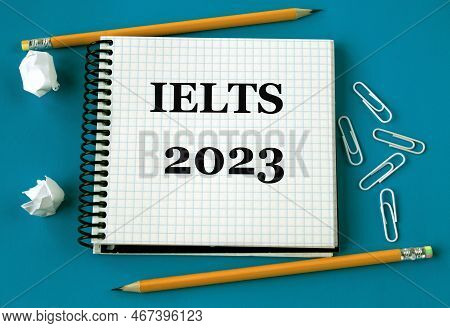 Ielts 2023 - Word In A White Notebook On A Blue Background With Pencils, Paper Clips. Education Conc