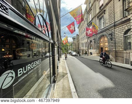 Geneva, Switzerland - September 15 2021: A Cyclist Is Riding On A Small Old Town Street With Nationa