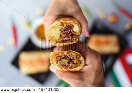 Hands Holding Mexican Burritos With Chorizo, Potato, Cheese And Beef Served With Sauce Barracha
