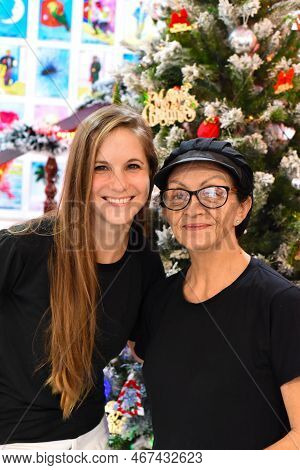 Young Slovak Woman Hugging With Senior Mexican Woman Standing Together Against Christmas Tree