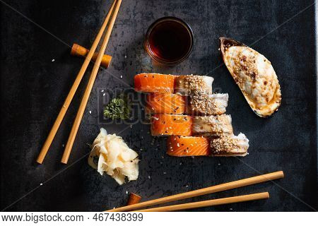 Sushi, Rolls And Baked Mussels On A Dark Background With Chinese Chopsticks Top View. Healthy Seafoo