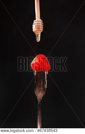 Half Of A Strawberry On An Old Fork On A Dark Background Close-up. Honey Flows Over Strawberries.