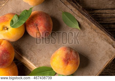 Peaches With Green Leaves Lie On A Book And A Wooden Background. Ripe Peaches Close-up On An Old Woo