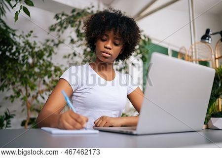 Low-angle View Of Focused African-american Young Woman Writing Information On Notebook With Pen, Lea