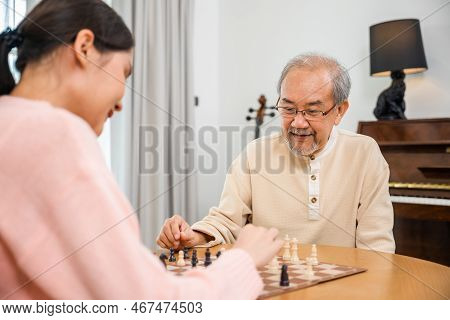 Smiling Senior Elderly Having Fun Playing Chess Game With Beautiful Daughter At Home, Nurse Caregive