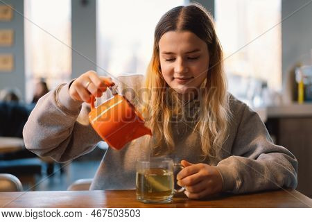 Portrait Of A Joyful Teengirl Enjoying A Cup Of Tea At Cafe. Smiling Beautiful Girl Drinks Hot Tea I