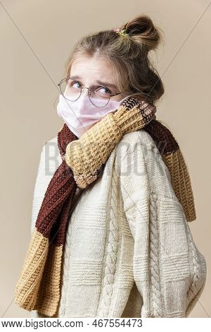 Caucasian Blond Female Girl In Glasses Wearing Warm Knitted Sweater And Winter Scarf In Facial Prote