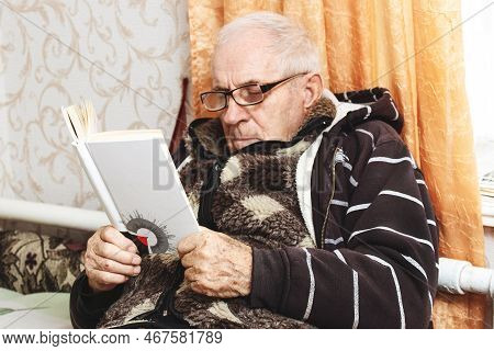 Ukraine, Khmelnytskyi, December 2022. Old Grandfather On The Sofa With A Book In His Hands. Leisure 