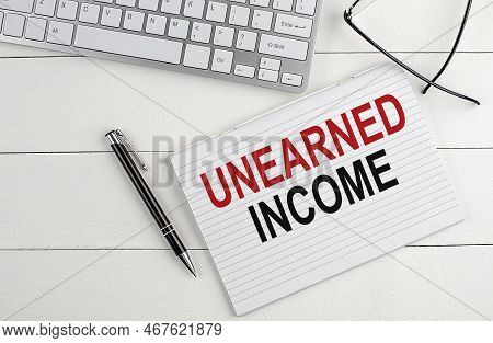 Unearned Income Text On Notebook With Keyboard , Pen Glasses On A White Wooden Background