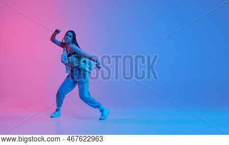 Young Sportive Girl Dancing Over Gradient Pink Blue Background In Neon Light. Hip-hop Culture