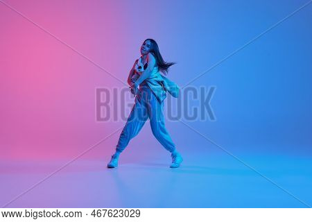 Catch The Rhythm. Young Stylish Girl Dancing Hip-hop Over Gradient Pink Blue Background In Neon Ligh
