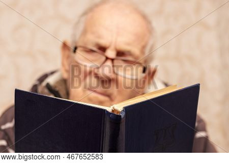 Ukraine, Khmelnytskyi, December 2022. Grandfather In Glasses Reads A Book In The Room. Leisure For T