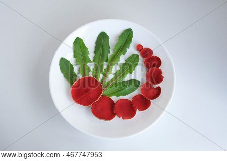 Sarcoscypha Coccinea Mushrooms Lie With The Leaves Of The Taraxacum Plant On A Round, White Plate. T