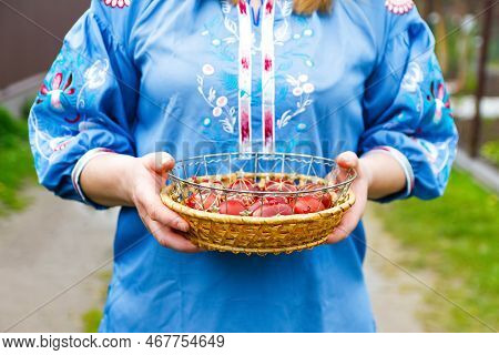 Defocus Female Hands Holding Basket Of Colored Red Eggs On Nature Green Grass Background. Easter Hol