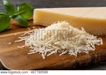 Heap Of Grated Grana Padano Cheese Closeup. Tasty Parmesan Grated And Whole Wedge Over Wooden Cuttin
