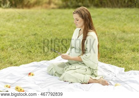 Young Pretty Pregnant Girl Holding, Reading Something On Tablet, Gadget, Resting In Park, Sitting On