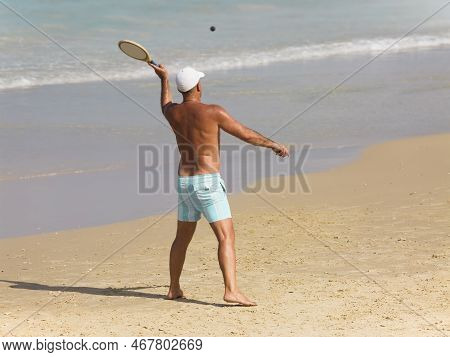 A Tanned Athletic Man Plays Matkot Against The Background Of The Sea