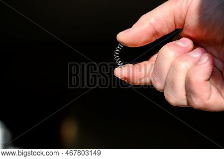 Caucasian Hand Compressing A Metal Spring Between A Thumb And Finger