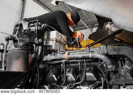 Car Mechanic Repairs Large Truck Or Tractor In Workshop. Professional Mechanic Repairs Truck Engine.