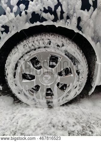 Car Wheel In White Washing Foam With Bubbles At Car Wash Close-up