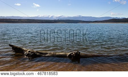 View Of The Barcena Reservoir With The Montes Aquilanos Mountain Range At Background And A Driftwood