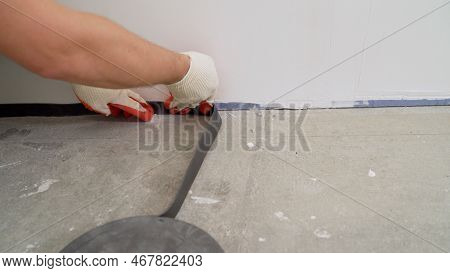 The Man Glues A Damping Tape On A Wall Bottom, Protection For A Floor Coupler. The Damping Tape Is G