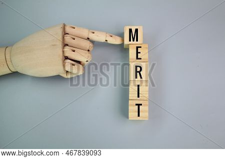 A Wooden Hand Pushes A Wooden Cube With The Word Merit. The Quality Of Being Particularly Good Or Wo