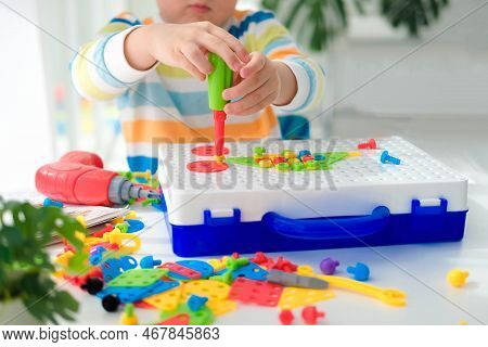 Little Boy Playing Set With A Screwdriver And A Drill,  And Screws And Parts . The Child Plays Build