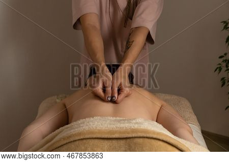 Masseur Does A Back Massage Standing At The Head Of A Woman Lying On A Massage Couch In A Warm Atmos