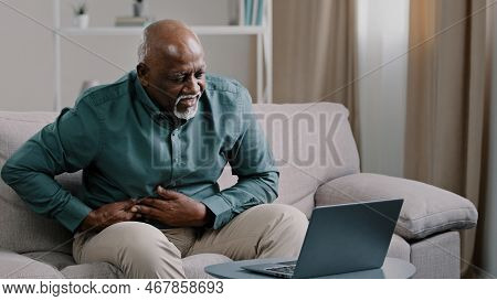 Older African American Male Freelancer Mature Pensioner Sitting At Home Office On Couch Using Laptop