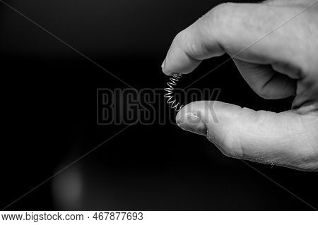 Caucasian Hand Compressing A Metal Spring Between A Thumb And Finger