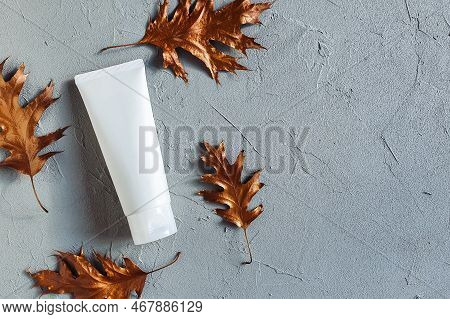 White Squeeze Bottle Cosmetic Tube Pack And Copper Color Oak Leaf On Gray Concrete Texture Backgroun
