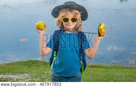 Cute Blond Kid With Camera Wearing Explorer Hat And Backpack On Nature. Child Explorer Hiking And Ad