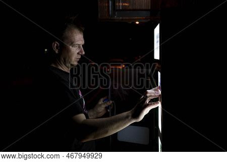 Man Drawing Clean Water From A Water Vending Machine On A Dark Night, Foreground And Background Blur