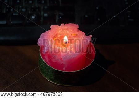 Burning Thick Short Red Candle On The Table Against The Keyboard During A Blackout
