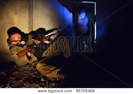 Soldier With The Rifle In The Gas Mask On The Foreground. Bloody Zombie In The Dark.