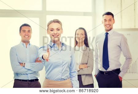 business and office concept - smiling beautiful businesswoman ready for handshake with team in office