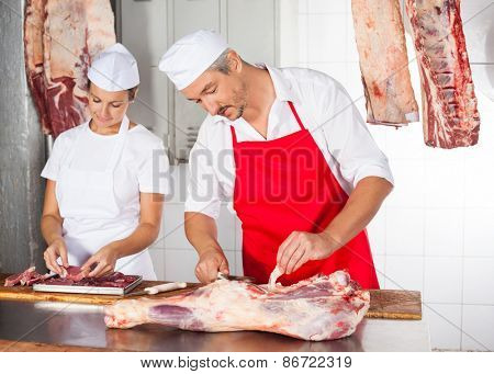 Mature male and female butchers working at counter in shop