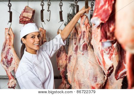 Portrait of mid adult female butcher hanging meat in butchery