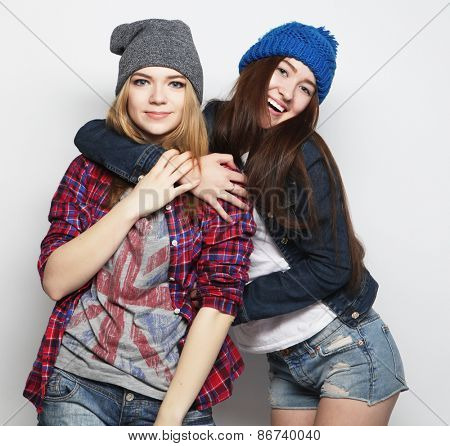 Fashion portrait of two stylish sexy hipster girls best friends, wearing cute swag outfits and hats. Over gray backround.