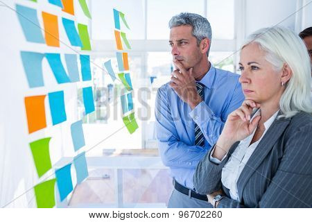 Business people looking at post it on the wall in office