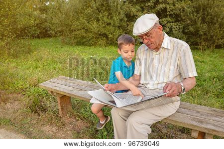 Senior man and child reading a newspaper outdoors