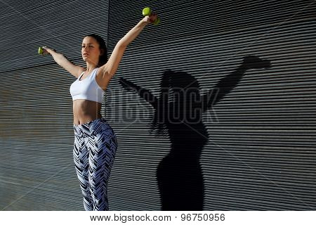 Beautiful young woman in sporty clothing training bicep curls while lifting weights outdoors