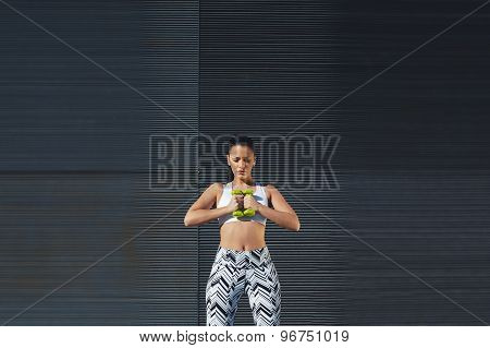 Gorgeous woman in workout gear holding weights with her hands together while training outdoors