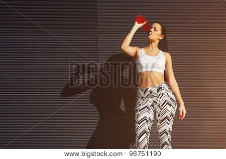 Female runner in workout clothes refreshing with energy drink during exercise outdoors in city