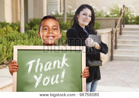 Happy Hispanic Boy Holding Thank You Chalk Board Outside on School Campus as Teacher Looks On.