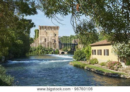 BORGHETTO, ITALY - JULY 11: Ruin of tower at Visconteo bridge, framed by vegetation and coasted by river Mincio. July 11, 2015 in Borghetto.