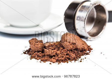 Spent or used coffee grounds with portafilter and a cup of freshly brewed coffee in the background