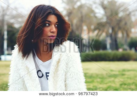 Portrait of attractive afro american woman with brunette hair sitting in the park with copy space