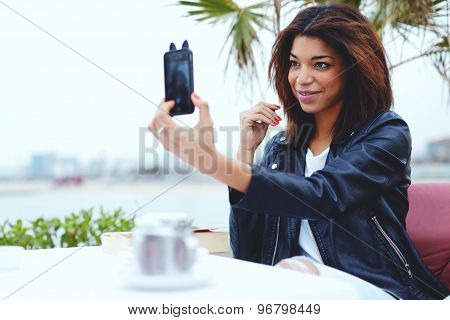Female taking a picture of herself on smartphone while sitting in coffee shop at her recreation time